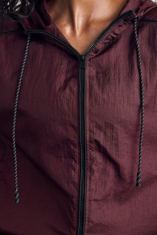 Close-up of a person wearing a lightweight hooded zip jacket in deep burgundy with black drawstrings and a black front zipper.