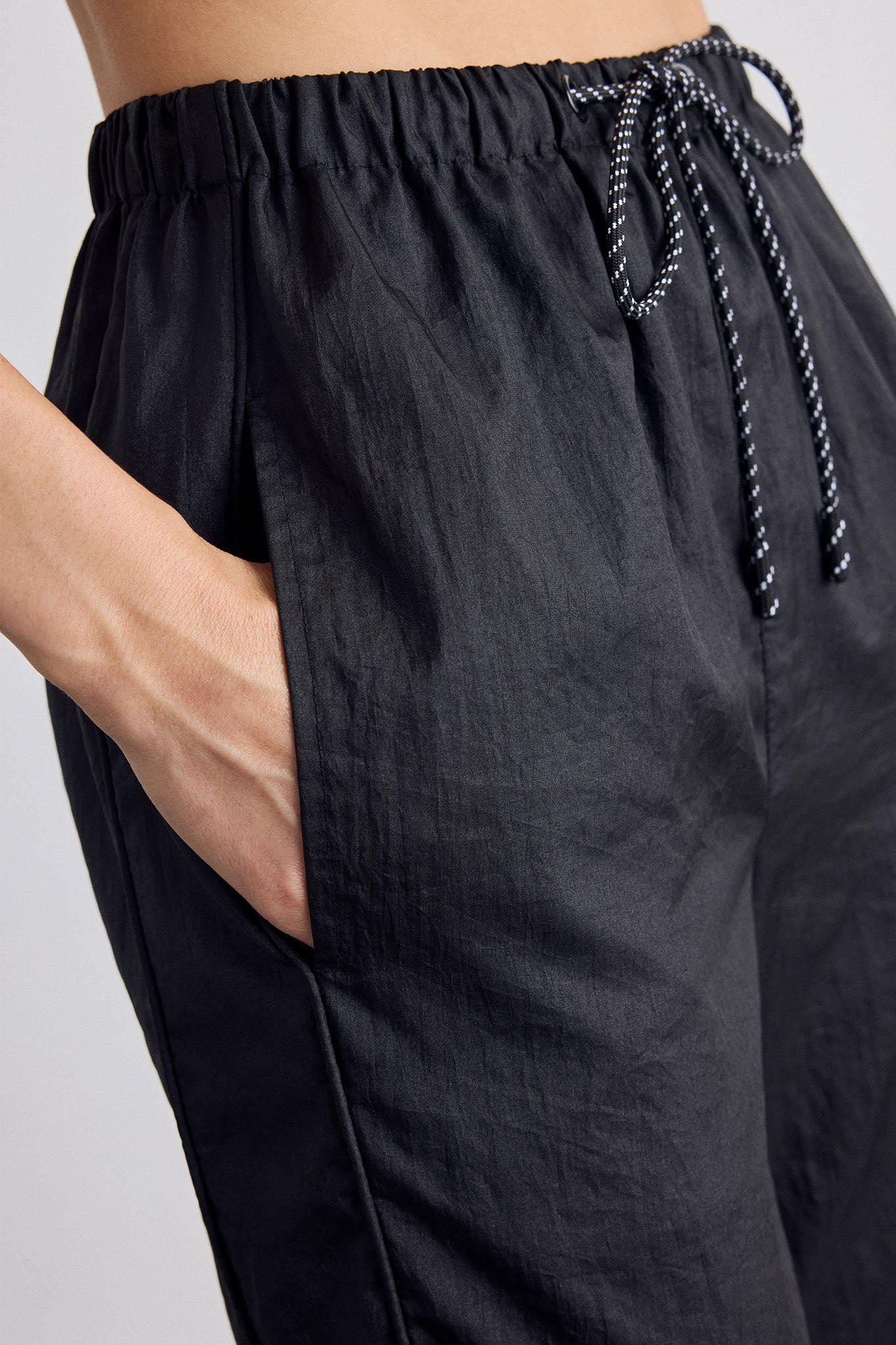 Close-up of a person wearing black drawstring pants with side pockets and a textured fabric, shown against a light gray background.