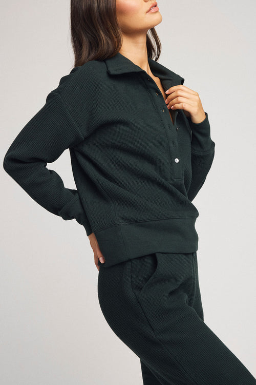 Dark teal waffle-knit pullover with half-button placket and long sleeves, side view