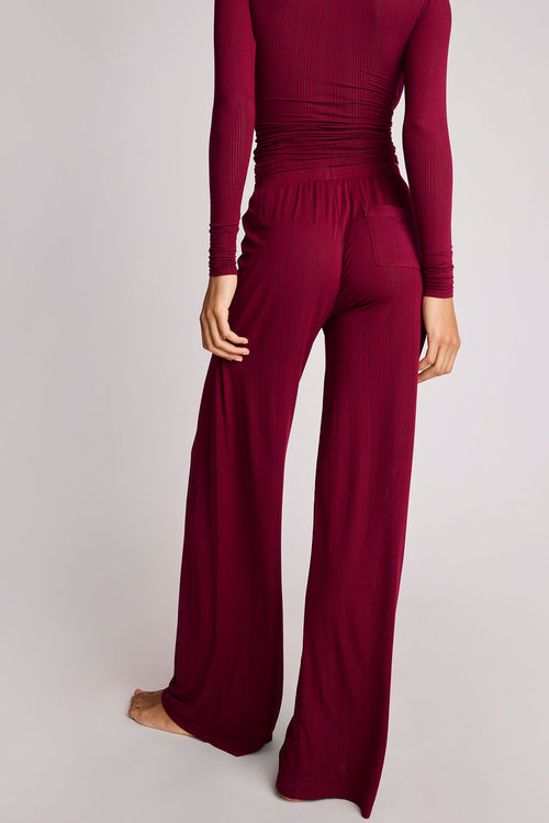 A person shown from the back wearing a matching long-sleeve ribbed top and wide-leg pants in a deep burgundy or wine color, photographed against a plain light gray studio background.