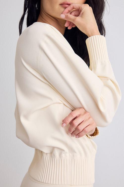 A close-up of a woman wearing a cream-colored bomber with ribbed cuffs and hem, shown from the side against a light gray background.