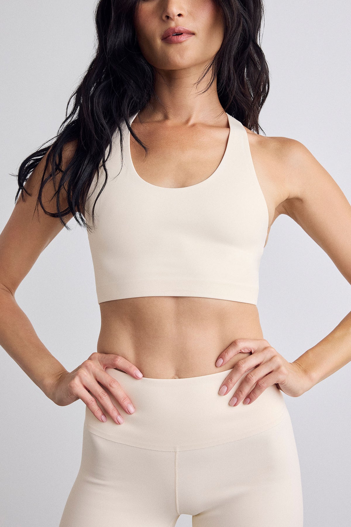 A woman wearing a matching cream sports bra and high-waisted leggings set, shown against a light gray studio background.