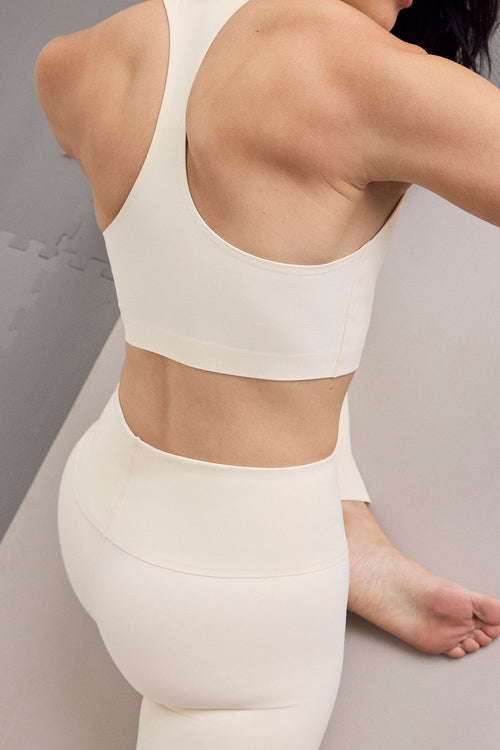 A close-up back view of a person wearing a matching cream-colored sports bra and high-waisted leggings set in a studio setting.