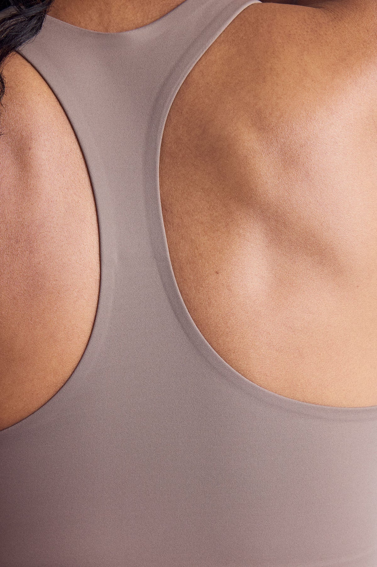 Close-up back view of a person wearing a smooth, solid taupe-gray racerback sports bra.