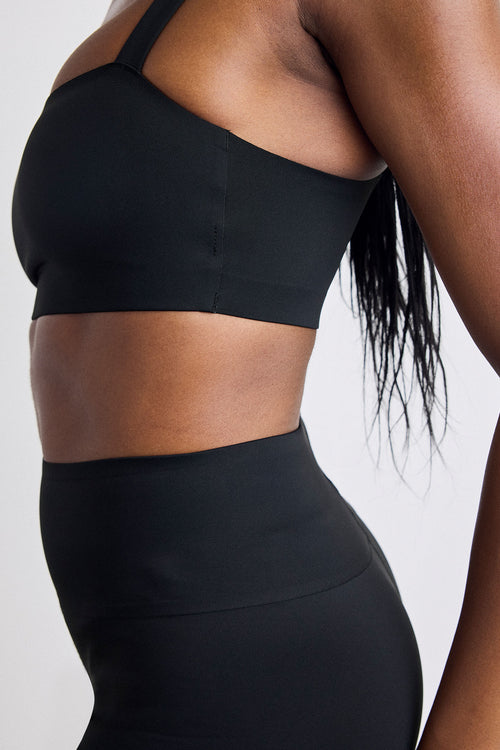 Close-up of a model wearing a black sports bra and matching high-waisted leggings against a light gray background.